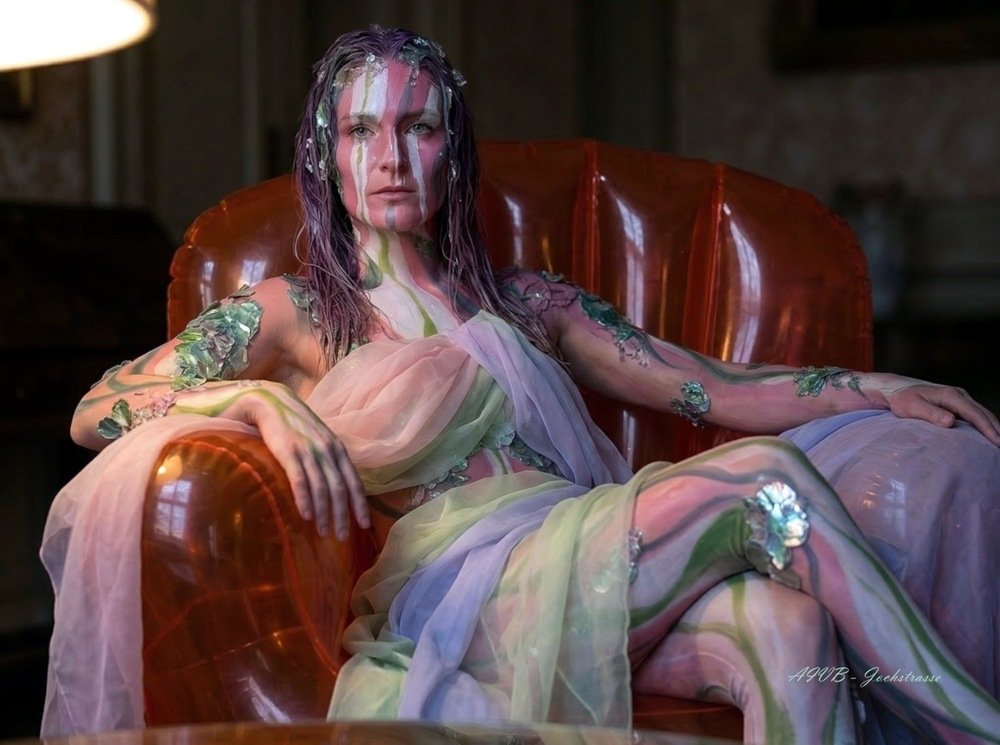 Autoportrait photographique d'Artemis Irenäus von Baste, 'Arty', en costume d'art vivant avec body painting floral, assise dans son fauteuil gonflable orange à Coire (Chur), Suisse, pour l'exposition Néo-Folklorisme Contemporain.