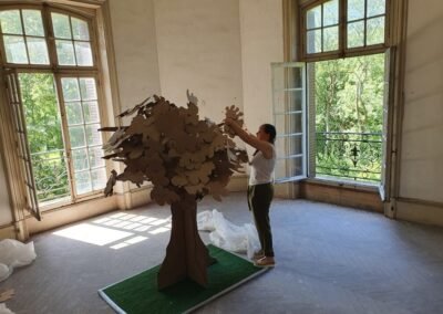 L'artiste Isabelle Morin assemblant son arbre en carton brut dans un salon en ruine au château du Bois-la-Croix